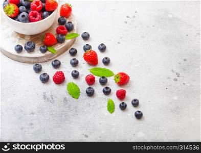 Fresh raw organic berries isolated in white ceramic bowl on round wooden board. Strawberry, Raspberry, Blueberry and Mint leaf