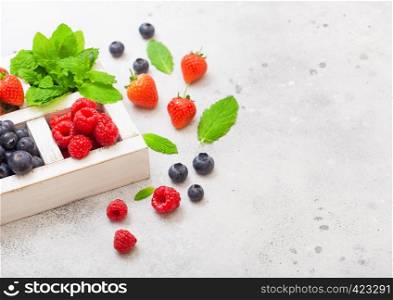 Fresh raw organic berries isolated in white wooden box on kitchen table background. Space for text. Strawberry, Raspberry, Blueberry and Mint leaf
