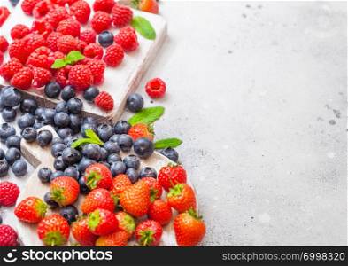 Fresh raw organic berries on vintage chopping boards on kitchen background. Space for text. Top view. Strawberry, Raspberry, Blueberry and Mint leaf