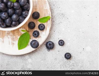 Fresh raw organic blueberries with leaf in white china bowl on kitchen background.