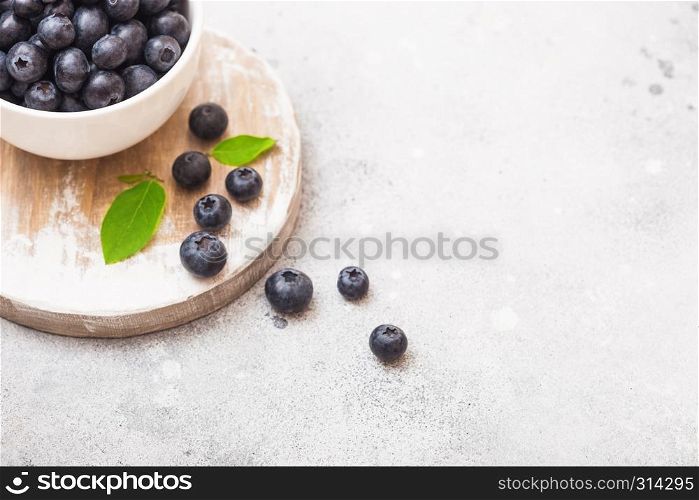 Fresh raw organic blueberries with leaf in white china bowl on kitchen background.