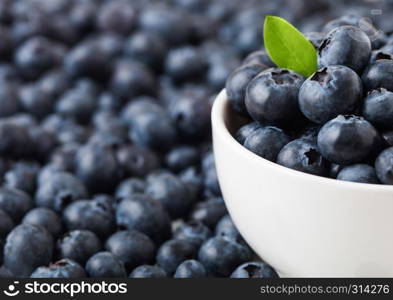 Fresh raw organic blueberries with leaf in white china bowl on white background. Macro