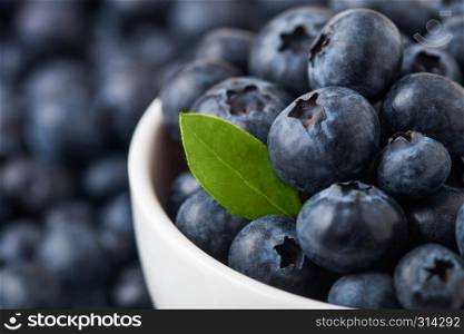 Fresh raw organic blueberries with leaf in white china bowl on white background. Macro