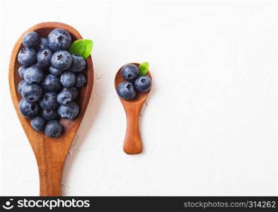 Fresh raw organic blueberries with leaf on large and mini wooden spoon on white kitchen background. Food concept.