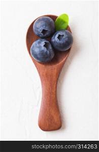 Fresh raw organic blueberries with leaf on mini wooden spoon on white kitchen background. Food concept.