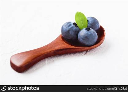 Fresh raw organic blueberries with leaf on mini wooden spoon on white kitchen background. Food concept.