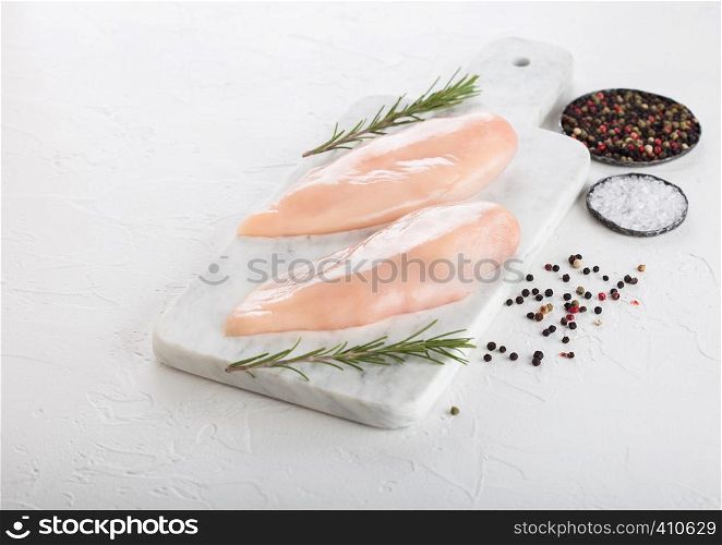 Fresh Raw Organic Chicken Fillet Breast on white marble board with spices and herbs on white.