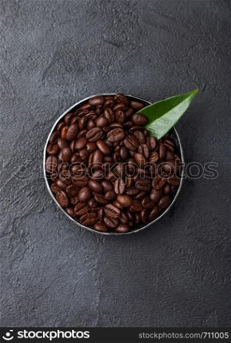 Fresh raw organic coffee beans in steel bowl with coffee trea leaf on black.