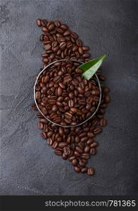 Fresh raw organic coffee beans in steel bowl with coffee trea leaf on black.