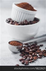 Fresh raw organic coffee beans in white bowl and powder on ligh table background and round steel scoop.