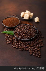 Fresh raw organic coffee beans with ground powder and cane sugar cubes with coffee trea leaf on brown.