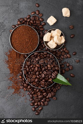 Fresh raw organic coffee beans with ground powder and cane sugar cubes with coffee trea leaf on black.