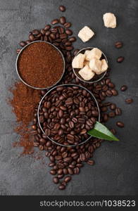 Fresh raw organic coffee beans with ground powder and cane sugar cubes with coffee trea leaf on black.