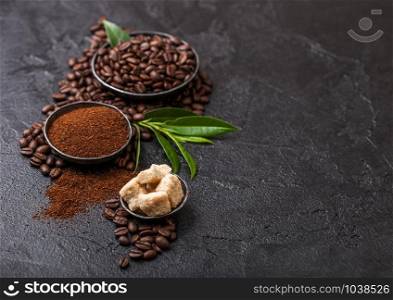 Fresh raw organic coffee beans with ground powder and cane sugar cubes with coffee trea leaf on black. Space for text.
