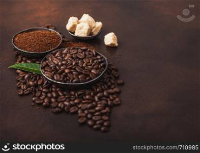 Fresh raw organic coffee beans with ground powder and cane sugar cubes with coffee trea leaf on brown. Space for text.