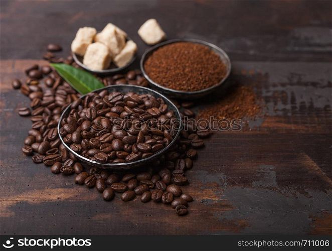 Fresh raw organic coffee beans with ground powder and cane sugar cubes with coffee trea leaf on wooden board.