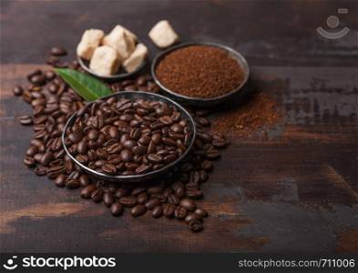 Fresh raw organic coffee beans with ground powder and cane sugar cubes with coffee trea leaf on wooden board.