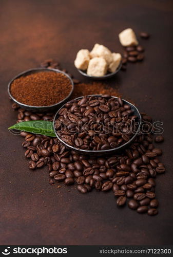 Fresh raw organic coffee beans with ground powder and cane sugar cubes with coffee trea leaf on brown.