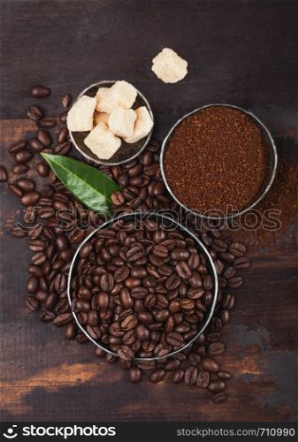Fresh raw organic coffee beans with ground powder and cane sugar cubes on wood.