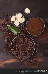 Fresh raw organic coffee beans with ground powder and cane sugar cubes on wood.