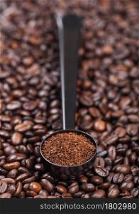 Fresh raw organic coffee powder in black steel scoop on top of coffee beans. Top view