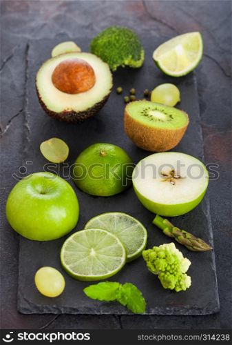Fresh raw organic green toned fruit and vegetables on stone board background. Avocado, lime, apple, kiwi and grapes with broccoli and cauliflower