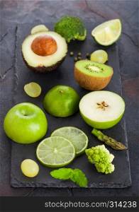Fresh raw organic green toned fruit and vegetables on stone board background. Avocado, lime, apple, kiwi and grapes with broccoli and cauliflower