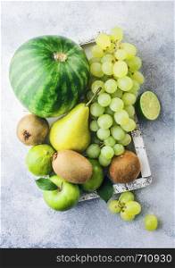 Fresh raw organic green toned fruit in white vintage box on stone kitchen table background. Watermelon, pear and grapes with kiwi and lime.