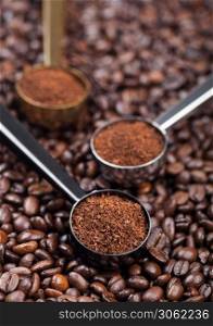 Fresh raw organic ground coffee powder in black, silver and golden steel scoops on top of coffee beans. Macro