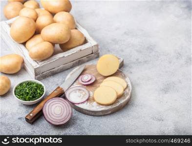 Fresh raw organic potatoes in wooden box and on chopping board with red and green onions on light background