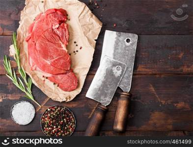 Fresh raw organic slice of braising steak fillet on chopping board with meat hatchets on wooden background. Space for text