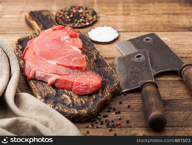 Fresh raw organic slice of braising steak fillet on chopping board with meat hatchets on wooden background.