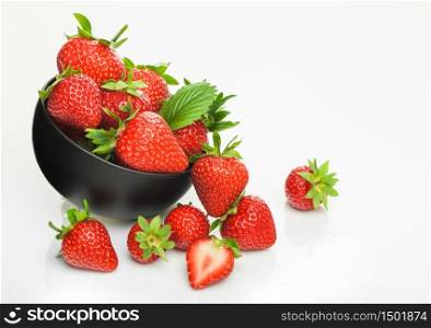 Fresh raw organic strawberries in black ceramic bowl plate on white background with berries next to it. Top view
