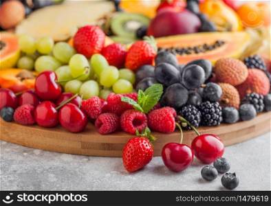 Fresh raw organic summer berries and exotic fruits in round large tray on light kitchen background. Papaya, grapes, nectarine, orange, raspberry, kiwi, strawberry, lychees, cherry. Top view