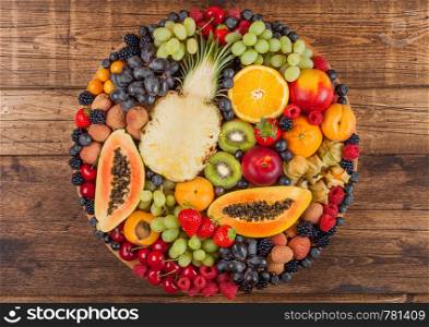 Fresh raw organic summer berries and exotic fruits in round large tray on wooden kitchen background. Papaya, grapes, nectarine, orange, raspberry, kiwi, strawberry, lychees, cherry.Top view