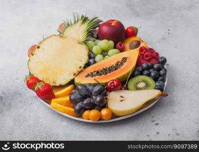 Fresh raw organic summer berries and exotic fruits in white plate on light background. Pineapple, papaya, grapes, nectarine, orange, apricot, kiwi, pear, lychees, cherry and physalis. Top view