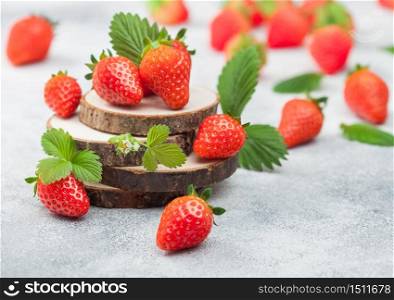 Fresh raw organic summer strawberries with a lot of vitamins and leaf on round timber boards on light table background.
