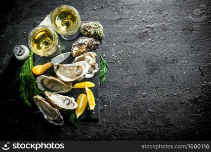 Fresh raw oysters on a stone Board with white wine. On black rustic background. Fresh raw oysters on a stone Board with white wine.