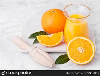 Fresh raw peeled oranges with hand wooden juice squeezer with leaves on white marble background