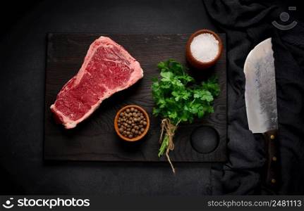 Fresh raw piece of beef meat, striploin steak on a black background, top view. Marbled piece of meat New York