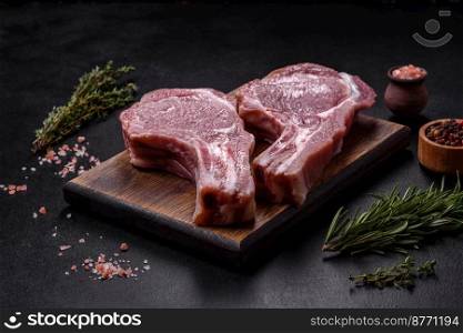 Fresh raw pork meat on the ribs with spices and herbs on a wooden cutting board on a dark concrete background