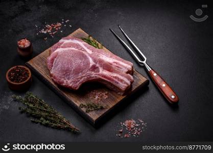Fresh raw pork meat on the ribs with spices and herbs on a wooden cutting board on a dark concrete background