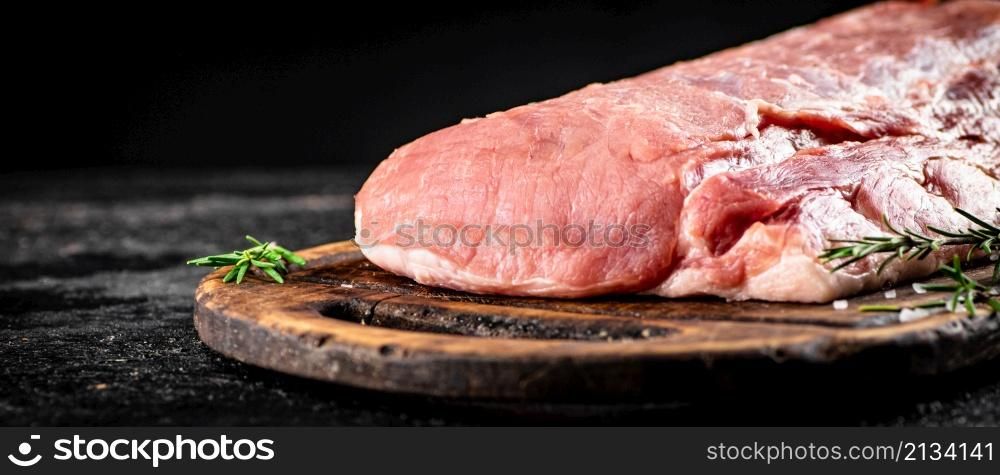 Fresh raw pork on a cutting board with rosemary. On a black background. High quality photo. Fresh raw pork on a cutting board with rosemary.