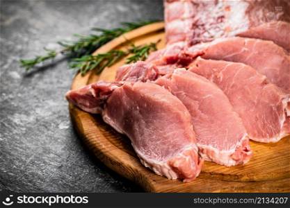 Fresh raw pork on a cutting board with rosemary. On a black background. High quality photo. Fresh raw pork on a cutting board with rosemary.