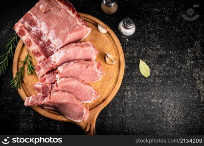 Fresh raw pork on a cutting board with rosemary. On a black background. High quality photo. Fresh raw pork on a cutting board with rosemary.