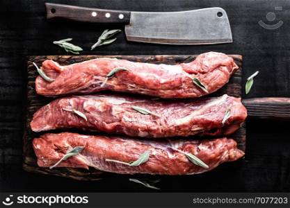 fresh raw pork tenderloin on wooden cutting board on dark background