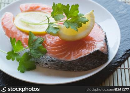 Fresh raw salmon cutlet with lemons and parsley garnish