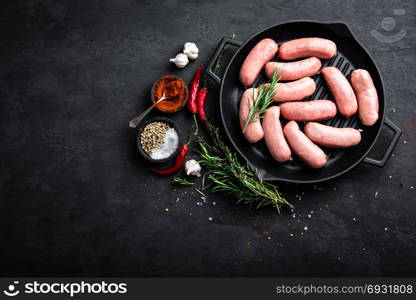 Fresh raw sausages on a cast-iron grill pan on a black background, top view