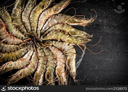 Fresh raw shrimp on a round stone board. On a black background. High quality photo. Fresh raw shrimp on a round stone board.