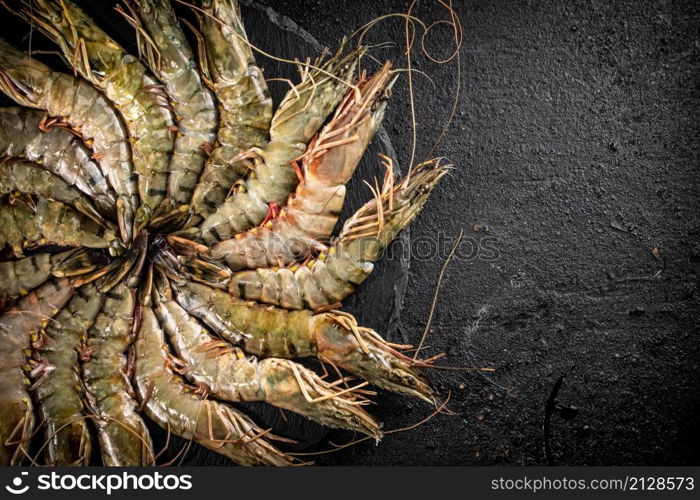 Fresh raw shrimp on a round stone board. On a black background. High quality photo. Fresh raw shrimp on a round stone board.